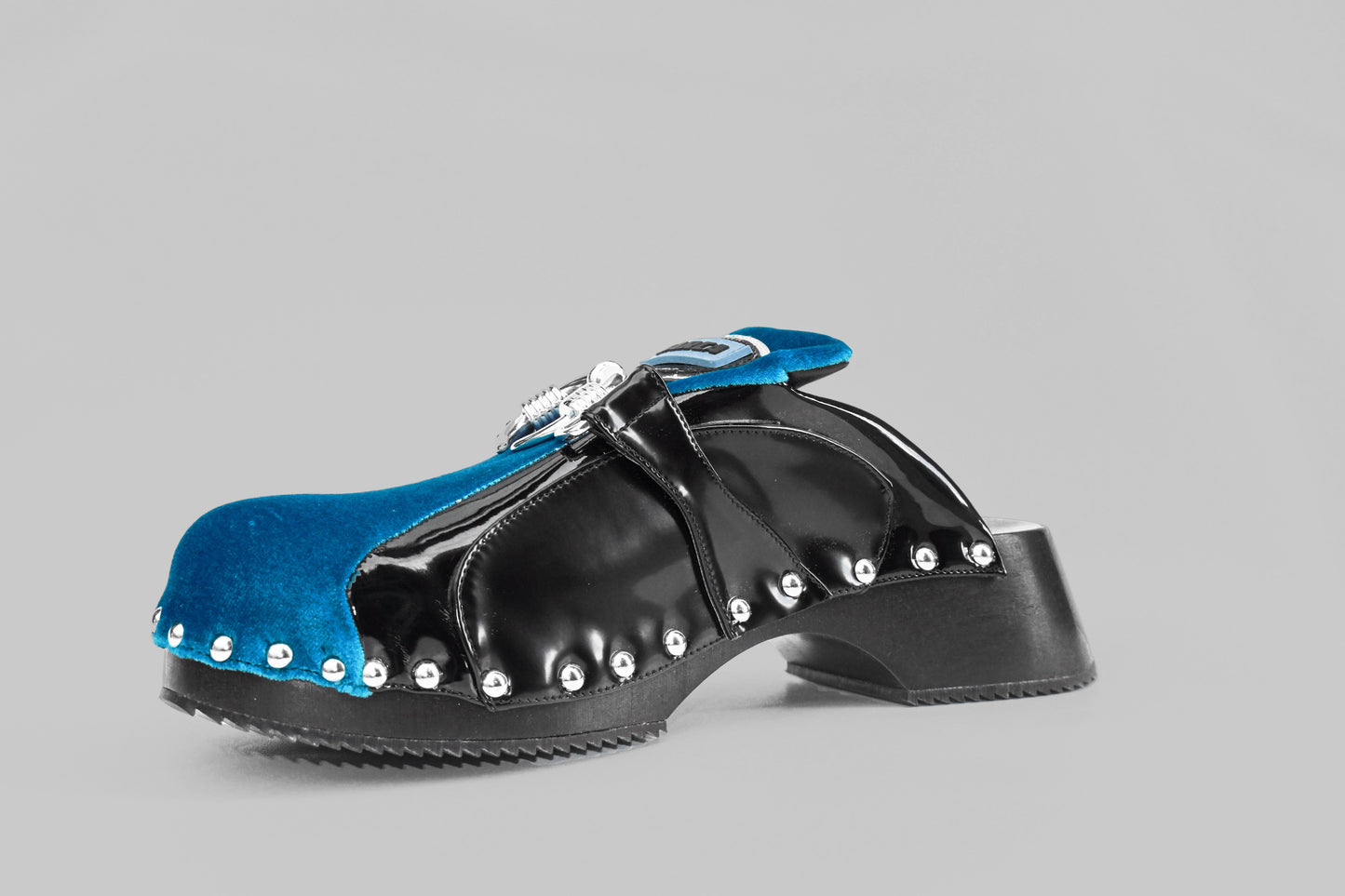 A photograph of the diagonal view of Ancuta Sarca blue back beetle clog, patent finish, velvet panel with ring embellishment, logo patch at tongues, branded footbeds, round toes, silver tone hardware, made in Italy. Unisex shoe.
