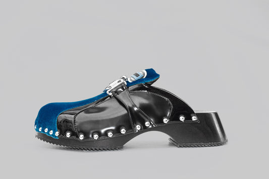 A photograph of the side view of Ancuta Sarca blue back beetle clog, patent finish, velvet panel with ring embellishment, logo patch at tongues, branded footbeds, round toes, silver tone hardware, made in Italy. Unisex shoe.