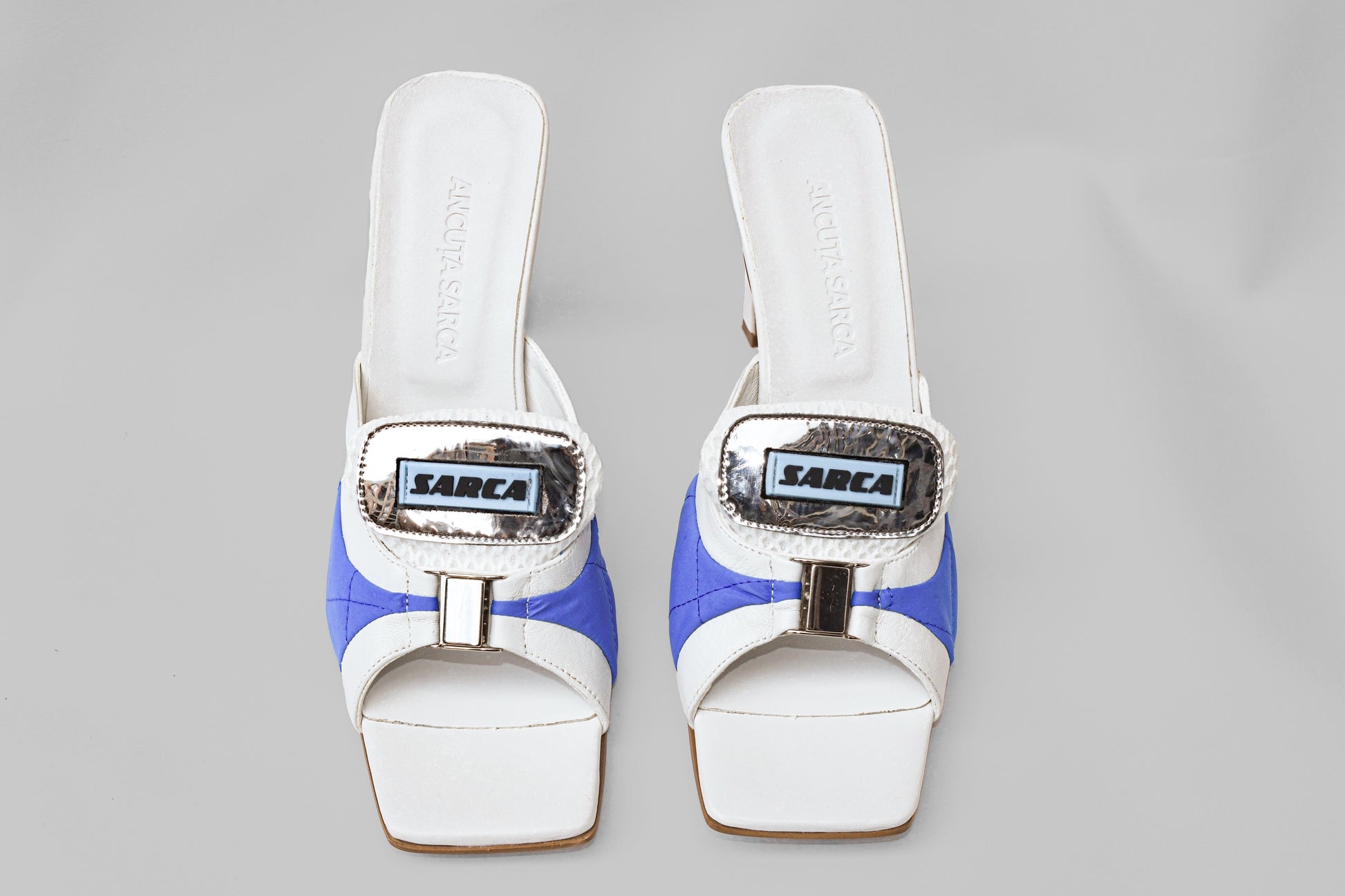 A photo of the top view of a pair of Ancuta Sarca Lithium Sandals, white and blue with 9CM HEEL, PANELLED DESIGN, SQUARE TOE, PADDED MESH TONGUE WITH LOGO PATCH, SILVER TONE HARDWARE, MADE IN ITALY